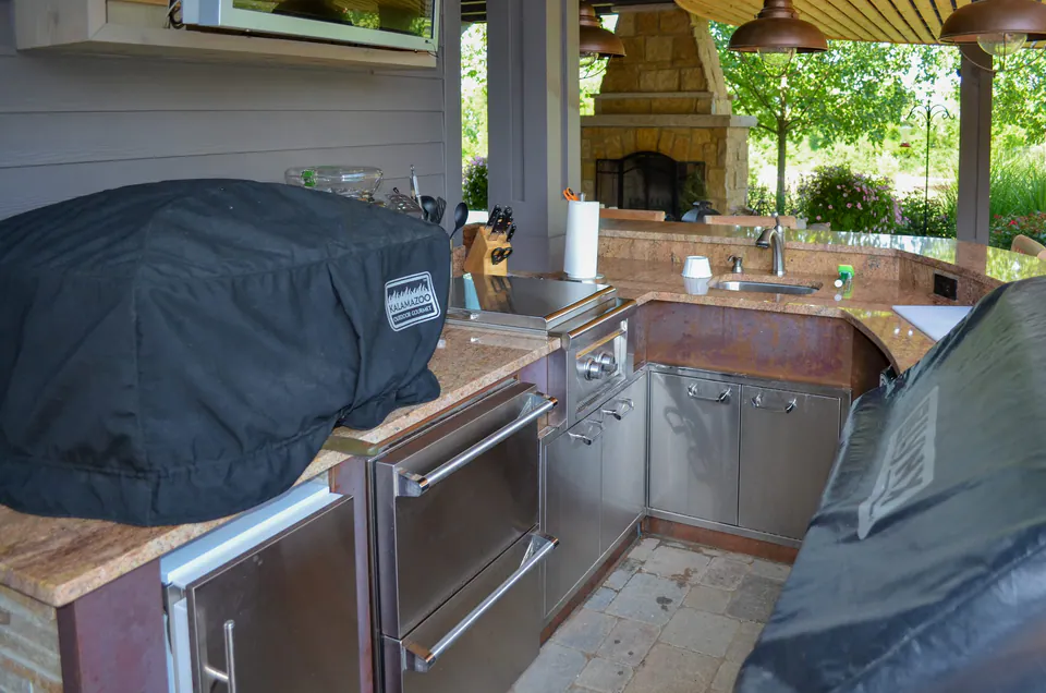 Close view of stainless outdoor grill, prep counter, storage drawers, sink, and covered kitchen workspace.